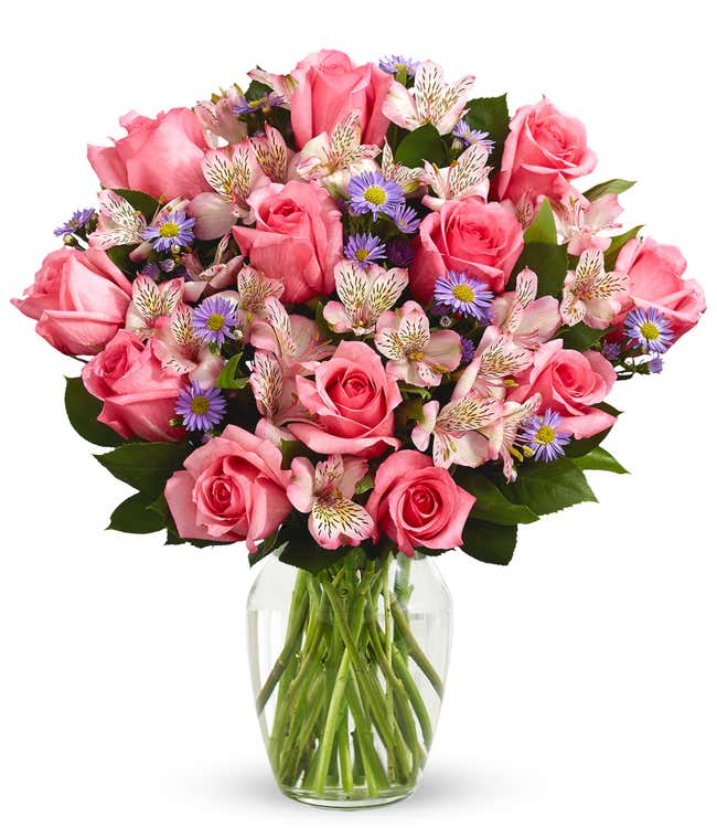 A bouquet of pink roses, white alstroemeria, and lavender aster in a glass vase 