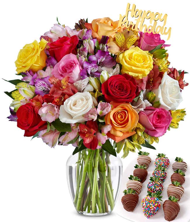 Deluxe birthday flower arrangement with mixed roses and vibrant alstroemeria in a clear glass vase, topped with a gold 