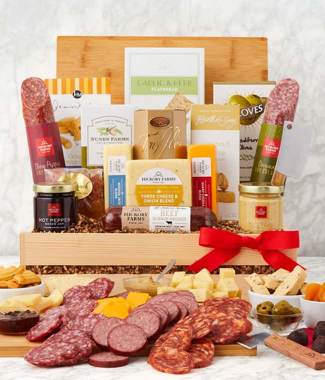 Gourmet charcuterie gift box with assorted salami, beef and turkey summer sausages, Three Cheese &amp; Onion Blend, crackers, garlic &amp; herb flatbread, hot pepper bacon jam, mustard, nuts, almond biscotti, and olives, arranged with a red bow.
