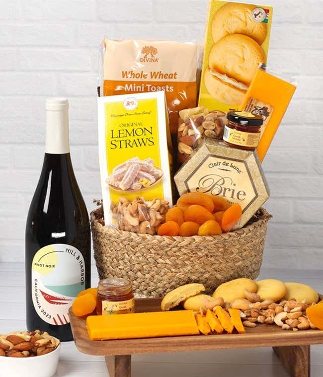 A two-toned woven basket filled with two cheeses, lemon flavored baked goods, crackers, dried apricots, gourmet nuts, and honey. 