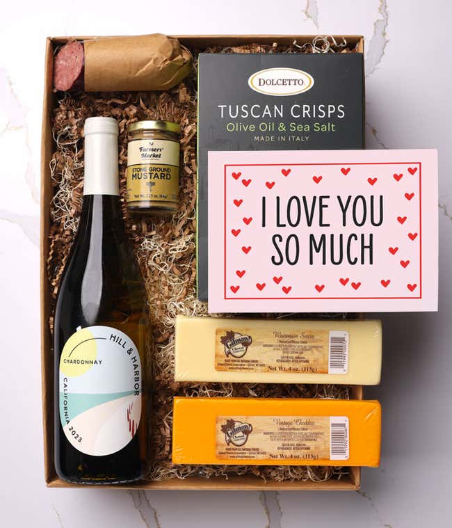 A beautifully arranged gift box featuring a bottle of Hill &amp; Harbor Pinot Noir, two hard cheeses, a jar of stone-ground mustard, gourmet crackers, savory summer sausage, and a pink card with hearts that reads 'I Love You So Much'