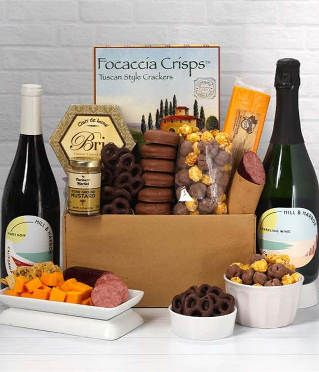 A gift set featuring 2 bottles of Hill &amp; Harbor wine - red and sparkling, focaccia crisps, 2 cheeses, mustard, summer sausage, caramel popcorn, chocolate pretzels, and 6 chocolate-covered Oreos for a sweet and savory gourmet experience.